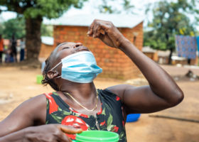在农村，一名妇女用药片盖住嘴巴，头向后仰着。她的另一只手拿着一杯水。
