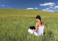 年轻女子拿着笔记本电脑躺在草地上